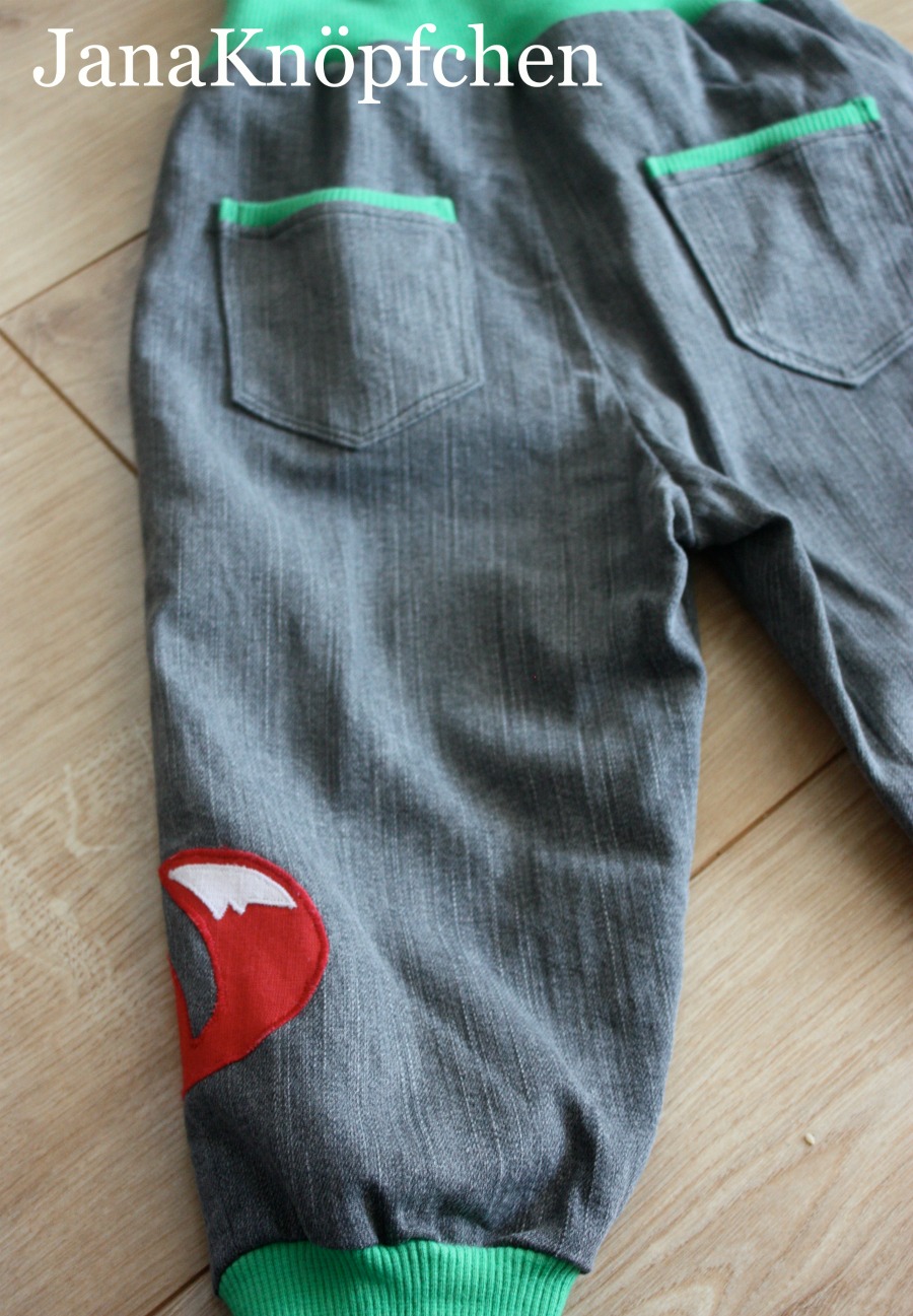Kinderhose aus grauem Jeans mit grünem Bündchen. Hinteransicht mit Gesäßtaschen und an der rechten Hosenbeinseite ist der Schwanz des Fuchses zu sehen